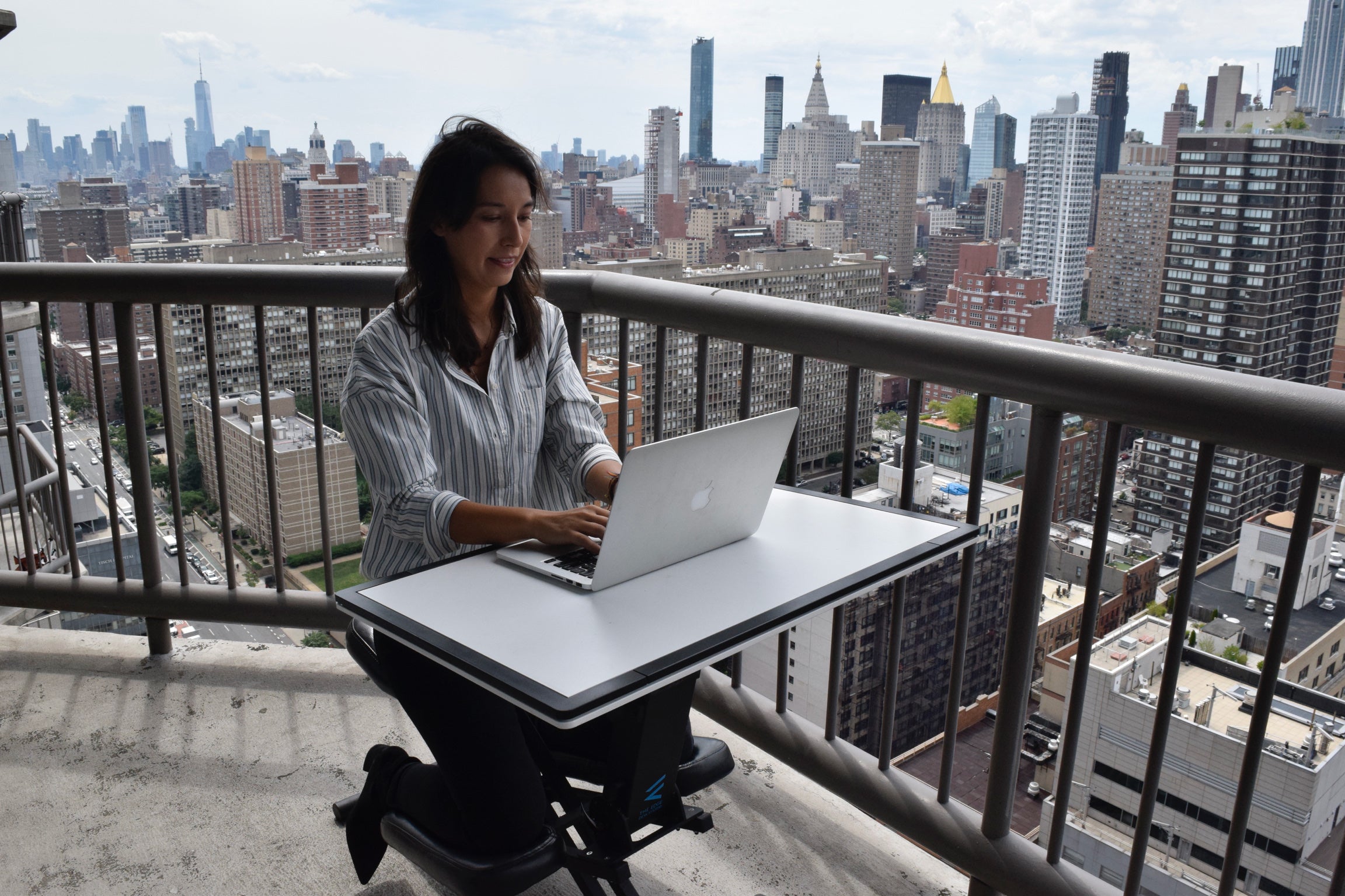 Woman happily using the edge desk ergonomic kneeling desk as an adjustable workstation on her balcony