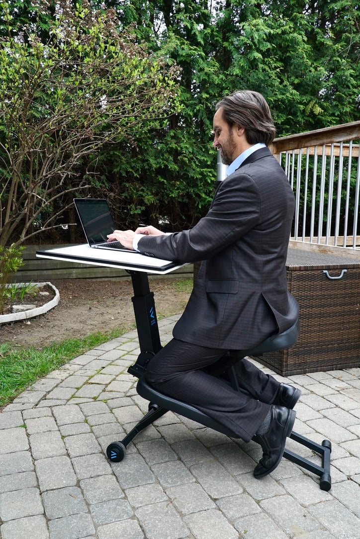 Man happily using the edge desk ergonomic kneeling desk as an adjustable workstation in his garden outside